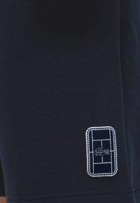 Gros plan sur un tissu bleu marine avec un petit logo de crocodile blanc brodé à l'intérieur d'un contour rectangulaire avec des bords cousus.