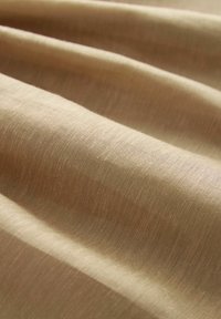 Beige szövet finom textúrával, amely lágy, folyó redőket mutat. A felületen finom fényesség és egy gyönyörű szövött minta látható.