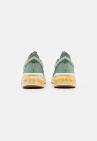 Pair of green athletic shoes with textured yellow soles, visible from the back on a plain white background.