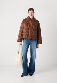 Jachetă neagră cu quilt, cu guler și nasturi, asortată cu blugi evazați albaștri, ținând o geantă albă, lejeră. Pantofi negri cu vârf ascuțit vizibili.