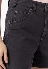 Mustat farkkushortsit, joissa on tekstuuri pintana, etutasku, metalliset yksityiskohdat ja näkyvät ompelusaumat.