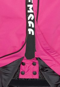 Fuchsia-Jacke mit schwarzem Futter, ausgestattet mit einem Reißverschluss und verstellbaren Druckknöpfen. Schwarze Riemen mit weißer Schrift entlang der Öffnung.