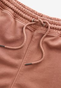 Gros plan sur la taille d'un pantalon de survêtement rose avec une bande élastique et un cordon noué avec des embouts métalliques.