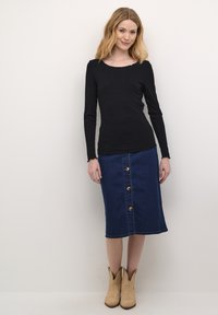 Maglia nera a coste con maniche lunghe abbinata a una gonna in denim scuro con chiusura a bottoni frontale e stivali alla caviglia marrone chiaro.