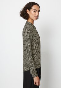 Blusa a maniche lunghe con motivo astratto nero e crema, dotata di colletto e dettaglio dei bottoni, realizzata in tessuto leggero e strutturato.
