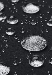 Jasné vodní kapky na texturovaném černém povrchu, různé velikosti, s hladkým, reflektivním povrchem, který zachycuje světlo a vytváří odrazy.