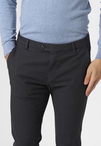 Pantaloni neri a fantasia con una vestibilità su misura, caratterizzati da una chiusura con un bottone e tasche laterali, abbinati a un maglione azzurro chiaro.