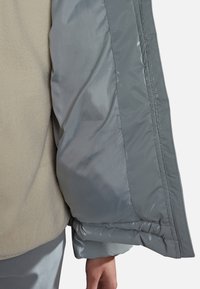 Puffertjakke med et lyst gråt nylon ydre og en blød, beige fleece indvendig, med samlede manchetter og en glat struktur.
