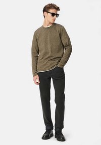 Pull texturé vert olive à col rond, associé à un pantalon noir et des chaussures noires à lacets. Le modèle porte des lunettes de soleil.