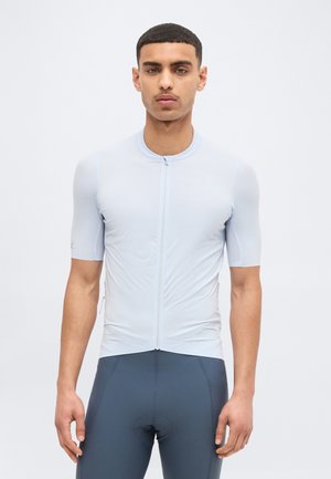 Νεαρός άνδρας που φοράει εφαρμοστή κοντομάνικη ποδηλατική φανέλα σε ανοιχτό μπλε χρώμα με φερμουάρ μπροστά και σκούρο γκρι ποδηλατικό σορτς.