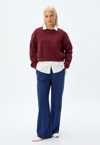 Maroonowy skrócony sweatshirt na białej koszuli, w zestawie z granatowymi spodniami o szerokich nogawkach. Białe buty dopełniają strój. Prosty krój i materiały.