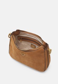 Bolso de ante marrón de Guess con cremallera dorada abierta, mostrando un forro interior beige con un bolsillo con cremallera y un parche con el logo de la marca.