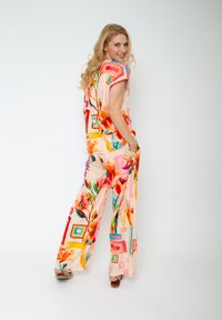 Farbiger Jumpsuit mit blühenden Mustern in Pink und Grün, versehen mit übergroßen Quadraten in lebhaften Farben, aus leichtem Stoff gefertigt.