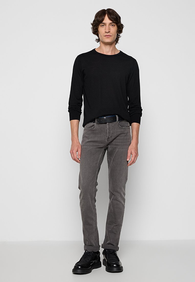 Schwarzes Langarmshirt kombiniert mit mittelgrauen Slim-Fit-Jeans und schwarzen Sneakern. Das Outfit zeichnet sich durch ein minimalistisches Design ohne sichtbare Logos aus.