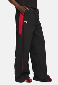 Pantalons noirs avec des accents rouges sur les côtés et un logo blanc. Présente une coupe ample et une taille élastique. Fabriqué en tissu léger.
