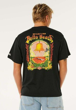 Man draagt een zwart T-shirt met een kleurrijk ontwerp van Bells Beach Australië, met op de achterkant een grote gouden bel, meeuwen, bloemen en vlammen.