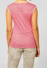 bezramínkový top v růžových a bílých horizontálních pruzích, s kulatým výstřihem a měkkou látkou, spárovaný se světle šedými texturovanými kalhotami.