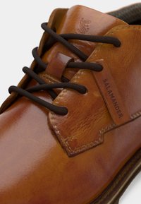 Scarpa in pelle marrone con una finitura lucida, caratterizzata da lacci marroni scuri, un design cucito e una piccola etichetta in legno con la scritta "SALAMANDER."