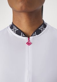 Prenda blanca con un cuello negro estampado y un tirador de cremallera rosa, que presenta un diseño moderno y una textura suave.