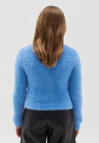 Blauwe fluffy trui met lange mouwen, aansluitend design en zachte textuur. Draag met zwarte leren broek, gezien vanuit de achterkant.