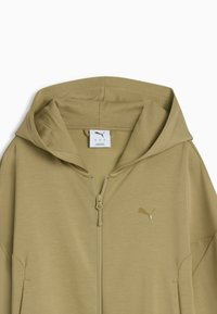 Sweat à capuche beige zippé Puma avec un petit logo Puma doré sur la poitrine et une étiquette blanche de la marque au niveau du cou à l'intérieur de la capuche.