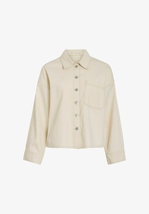 Chemise beige à manches longues avec col et poche poitrine, dotée de six boutons métalliques sur le devant.