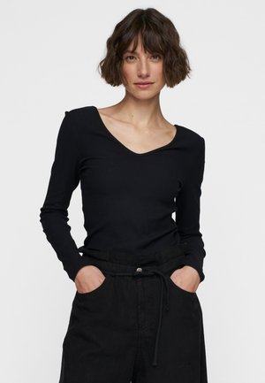 Black ribbed long-sleeve top with a wide V-neck and fitted silhouette. Paired with loose black trousers featuring a drawstring waist.
