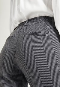 Spodnie w wzór jodełki w kolorze granatowym i białym. Posiadają płaski pas z gumką, tylną kieszeń oraz miękką, teksturowaną tkaninę.