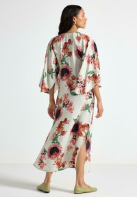 Maxi kjole med blomsterprint og løse kimonoærmer, der har en lys grå bundfarve med livlige pink, lilla og grønne nuancer. Slidsdetaljer i siden.