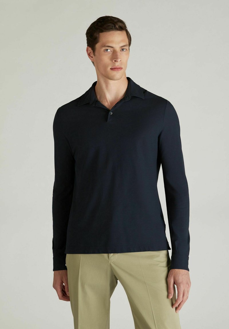 Polo à manches longues bleu marine avec un col classique, une patte de boutonnage à deux boutons et une texture lisse et douce. Assorti à un pantalon beige clair.