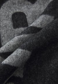Tissu noir et gris à motifs avec un tissage doux et texturé, comportant des formes abstraites et des nuances variées. Il semble chaleureux et confortable.