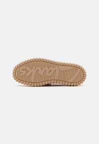 Semelle d'une basket en caoutchouc beige avec des stries texturées et un logo en relief. Présente des bords arrondis et un design solide et flexible.