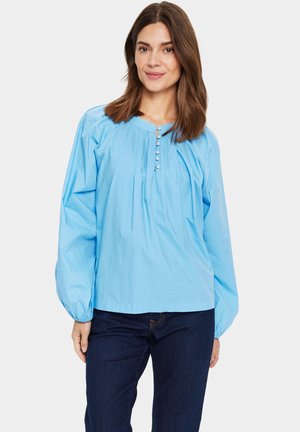 Blusa azzurro chiaro a maniche lunghe con scollo rotondo, pieghe sul davanti e dettagli con bottoni. Realizzata in un tessuto traspirante.