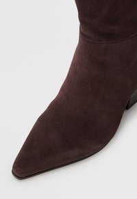 Bottine en suede marron avec un bout pointu et un talon court et épais. Texture lisse et détails de couture minimaux.