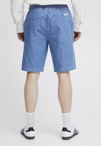 Pantalones cortos de mezclilla en azul claro con corte relajado. Cintura elástica, bolsillos traseros y dobladillos enrollados. Combinados con calcetines blancos y zapatillas.