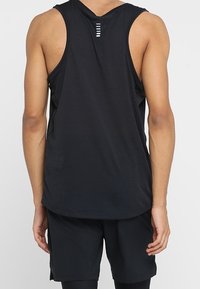 Débardeur de sport noir sans manches avec un ourlet arrondi, présentant un dos texturé et un détail de lignes horizontales près de l'encolure. Associé à un short noir.