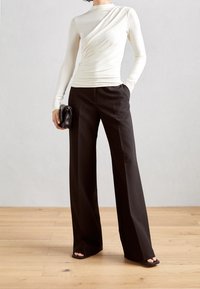 Krämfärgad långärmad topp med draperad detalj som matchas med svarta vida byxor. Anmärkningsvärt slät textur och figursydd silhuett. Svart clutch-accessoar.