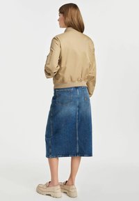 Beżowa kurtka bomberka z prążkowanymi mankietami i dołem, połączona z dżinsową spódnicą midi. Grube beżowe platformy dopełniają stylizację.