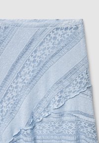 Écharpe bleu clair présentant des textures superposées, des motifs en dentelle florale et des bords en festons. Le tissu semble léger et doux.