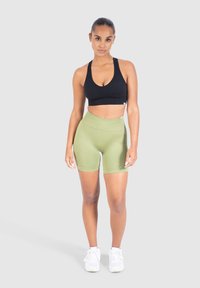 Svart sport-bh och olivgröna högmidjade shorts. Slät, elastisk tyg; figurnära design; kombinerad med vita träningsskor.