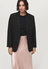 Black blazer with a tailored fit, single button closure, and two front pockets, paired with a textured, light pink satin skirt.