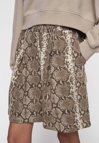 Falda de estampado de serpiente marrón con cinturilla elástica y bolsillos laterales. Fabricada en un material suave, con un patrón texturizado y un corte holgado.