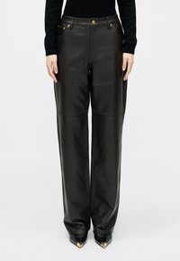 Črne široke usnjene hlače z zlatimi detajli, sprednjimi žepi in gladko teksturo, s vidnim šivanjem. Primerne za stilsk izgled.