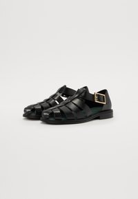 Zwarte leren sandalen met een geweven bovenstuk, open teen ontwerp, contrasterende gespsluiting en een platte zool. Soepele, glanzende textuur.