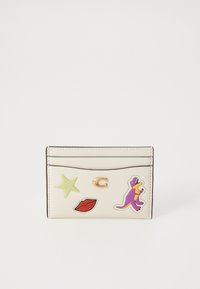 Kartenhalter aus cremefarbenem Leder mit dekorativen Aufklebern: ein grüner Stern, rote Lippen und ein lila Dinosaurier. Verfügt über ein goldenes "C"-Emblem.