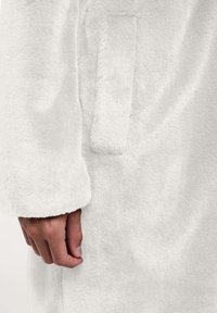 Witte, donzige fleecejas met een zachte textuur. Voorzien van een zijzak en ronde manchetten, ontworpen voor warmte en comfort.