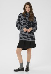 Prevelik sivi pulover z črnimi leopardjimi madeži, narejen iz mehkega materiala; kombiniran s črnimi nabranimi krilom in sijočimi črnimi loaferji.