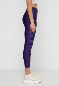 Leggings sportive viola con un motivo astratto testurizzato sui lati, realizzati in materiale elastico, progettati per comfort e prestazioni.