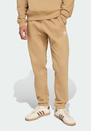 Beige sweatpants lavet af blødt stof, med sidelommer og et lille hvidt logo på venstre lår. Snittet har tapered ankler.