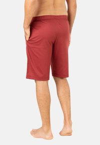 Shorts de sport bordeaux avec taille élastique. Texture lisse, longueur au genou, et poches latérales. Convient pour une tenue décontractée ou pour le sport.